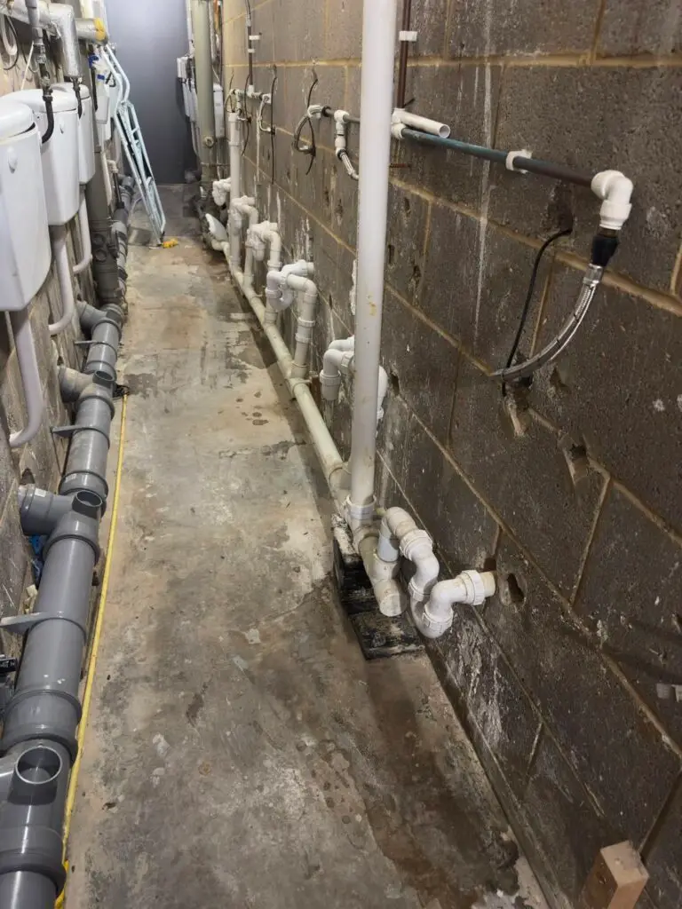 Service corridor behind a row of customer toilets at a retail park, showing the waste pipes and traps