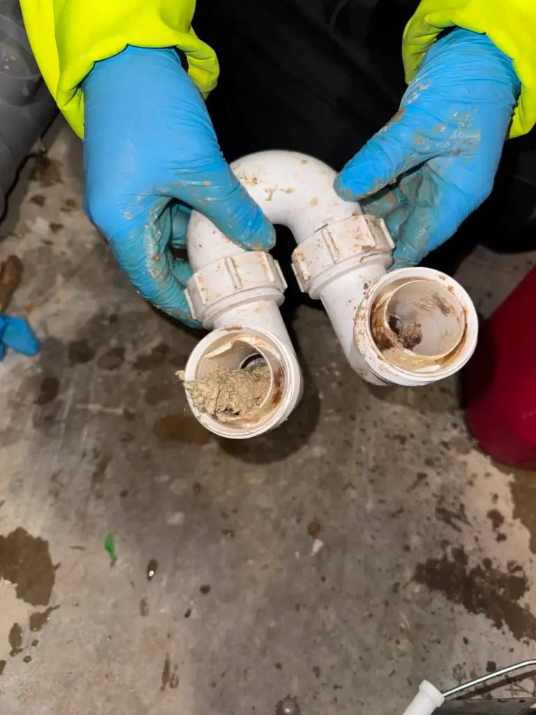 Blocked waste trap removed from a commercial washroom during planned drainage maintenance